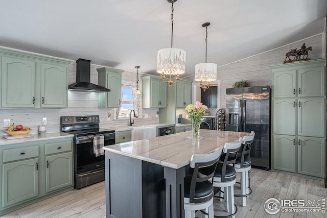 kitchen featuring green cabinets, appliances with stainless steel finishes, hanging light fixtures, a kitchen island, and wall chimney exhaust hood