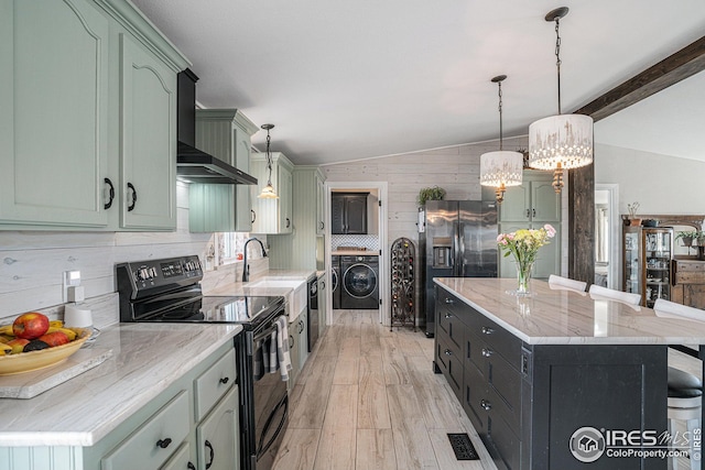 kitchen with decorative light fixtures, washer / dryer, stainless steel fridge, black range with electric stovetop, and wall chimney exhaust hood