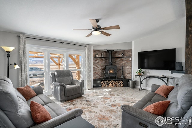 living room with ceiling fan, a wood stove, and light hardwood / wood-style floors