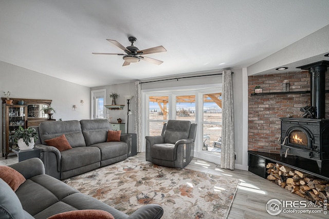 living room with light hardwood / wood-style flooring, a wood stove, ceiling fan, and vaulted ceiling