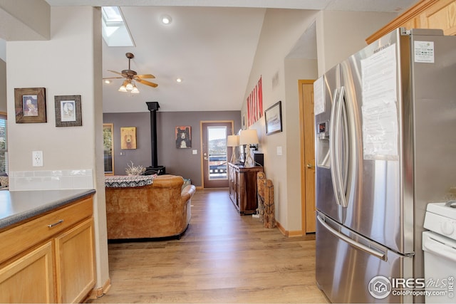 kitchen with stainless steel refrigerator with ice dispenser, a wood stove, light brown cabinetry, and light wood-type flooring