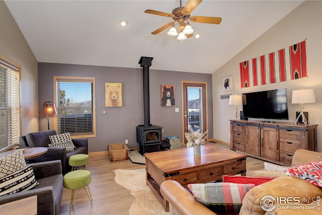 living room with vaulted ceiling, a wood stove, ceiling fan, and light wood-type flooring