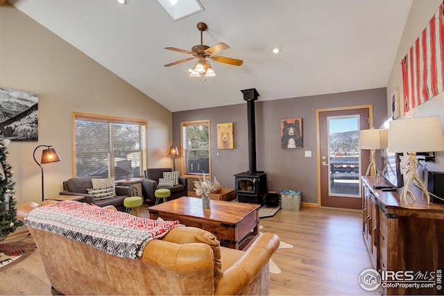 living room featuring ceiling fan, high vaulted ceiling, light hardwood / wood-style floors, and a wood stove