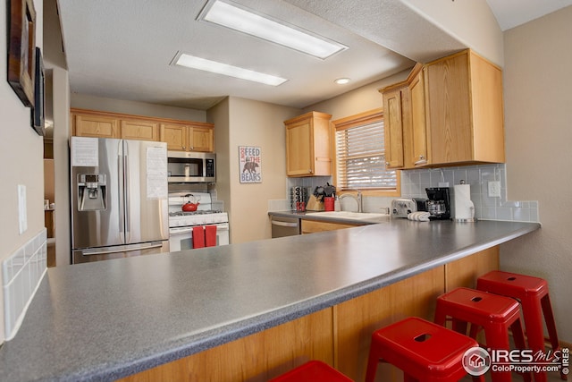 kitchen with a kitchen bar, sink, kitchen peninsula, and appliances with stainless steel finishes