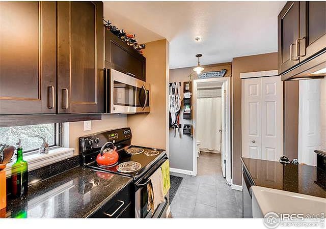 kitchen with pendant lighting, black electric range oven, dark stone countertops, light tile patterned floors, and dark brown cabinets