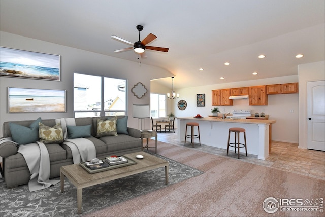 carpeted living room featuring ceiling fan with notable chandelier and vaulted ceiling