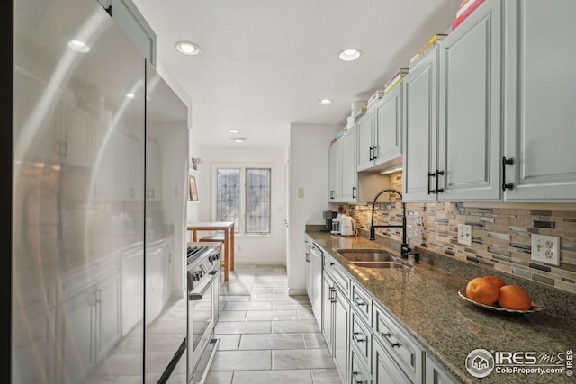 kitchen featuring stainless steel appliances, sink, backsplash, and dark stone counters