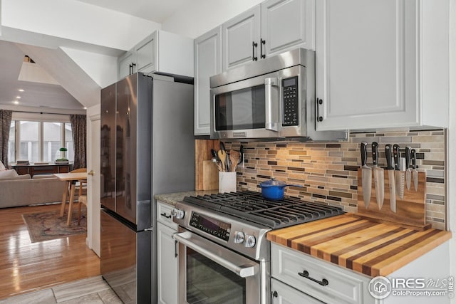 kitchen featuring appliances with stainless steel finishes, butcher block countertops, tasteful backsplash, white cabinets, and light wood-type flooring