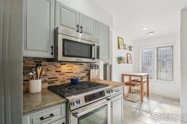 kitchen featuring dark stone countertops, tasteful backsplash, gray cabinetry, and appliances with stainless steel finishes