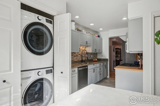 laundry area with hardwood / wood-style flooring, stacked washer and clothes dryer, and sink