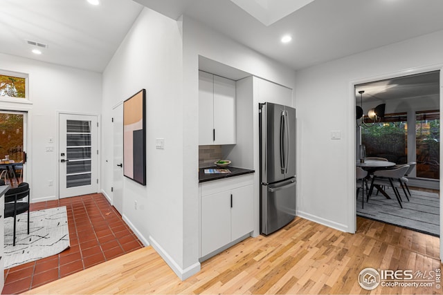 kitchen with white cabinetry, backsplash, light hardwood / wood-style flooring, and stainless steel refrigerator