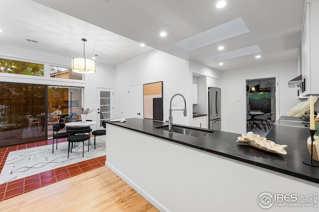 kitchen with sink, a skylight, stainless steel fridge, pendant lighting, and white cabinets