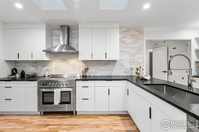 kitchen featuring sink, light hardwood / wood-style flooring, white cabinets, wall chimney exhaust hood, and stainless steel electric range