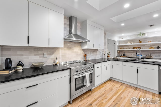 kitchen with sink, stainless steel electric range, white cabinetry, a skylight, and wall chimney exhaust hood