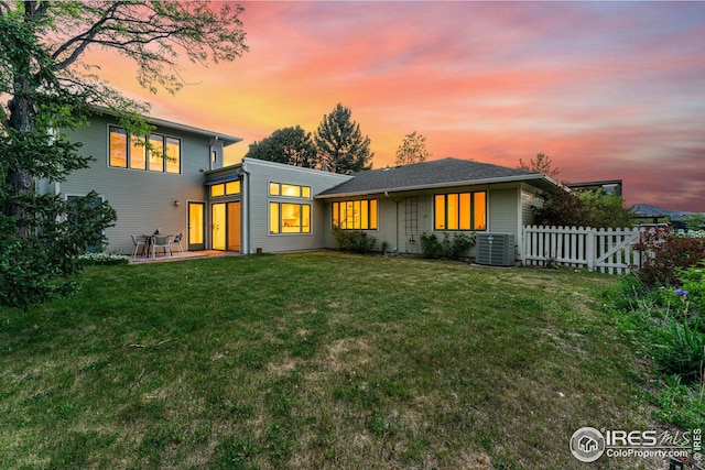 back house at dusk featuring central AC unit, a yard, and a patio area