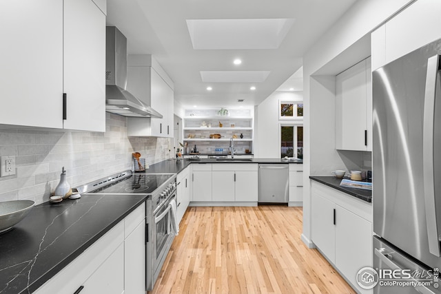 kitchen with a skylight, white cabinetry, sink, stainless steel appliances, and wall chimney exhaust hood