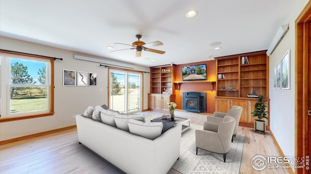 living room featuring built in shelves, ceiling fan, light wood-type flooring, and a wood stove