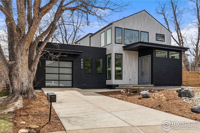 modern home with a garage, brick siding, concrete driveway, and fence