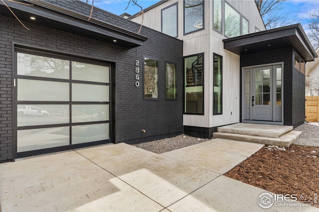 doorway to property featuring brick siding, concrete driveway, and an attached garage