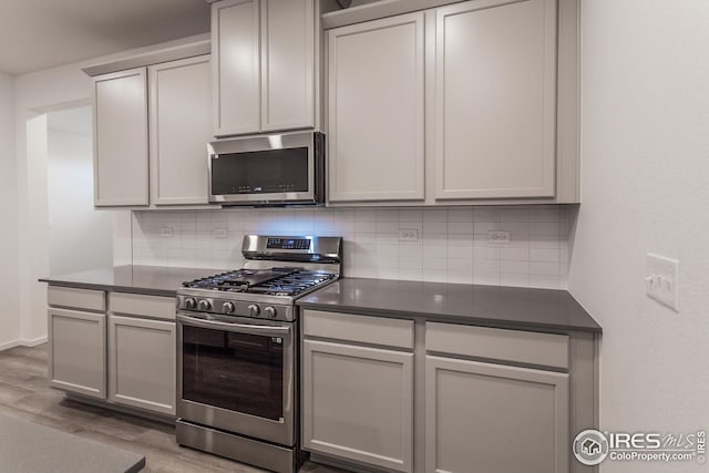 kitchen with backsplash, light wood-type flooring, gray cabinets, and appliances with stainless steel finishes