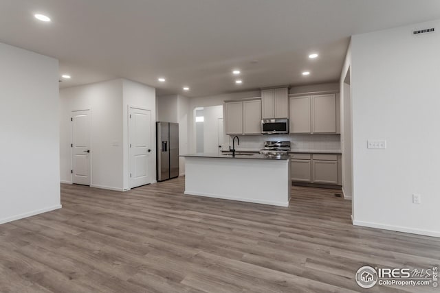 kitchen featuring a center island with sink, appliances with stainless steel finishes, gray cabinetry, and light hardwood / wood-style flooring