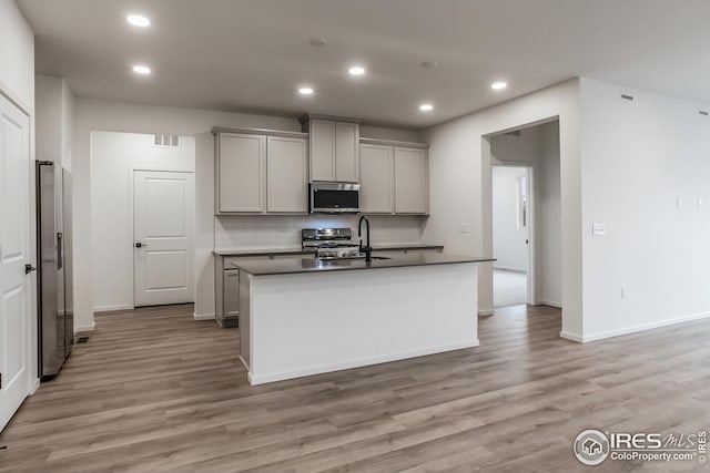 kitchen featuring stainless steel appliances, a center island with sink, sink, and gray cabinetry