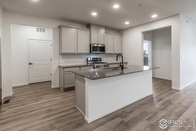 kitchen featuring sink, gray cabinets, appliances with stainless steel finishes, a kitchen island with sink, and backsplash