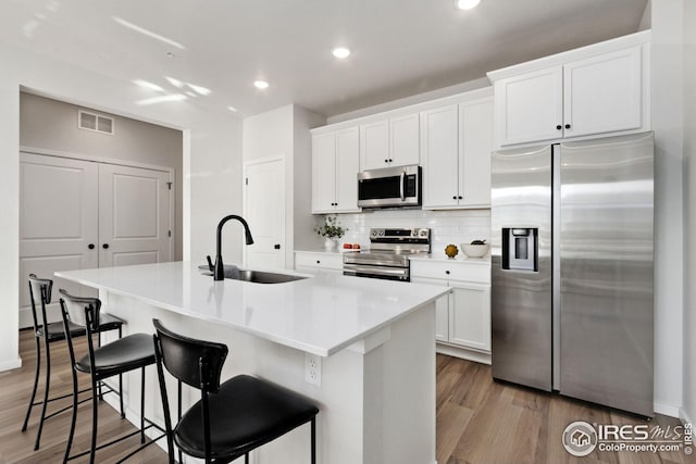 kitchen with white cabinetry, sink, a kitchen breakfast bar, stainless steel appliances, and a center island with sink