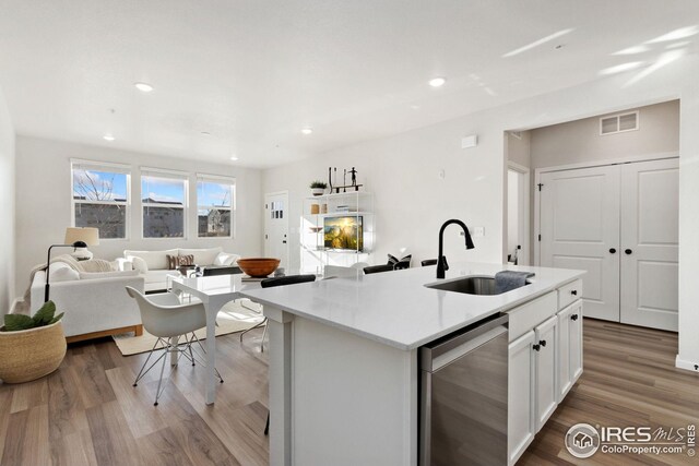 kitchen featuring sink, a center island with sink, light wood-type flooring, stainless steel dishwasher, and white cabinets