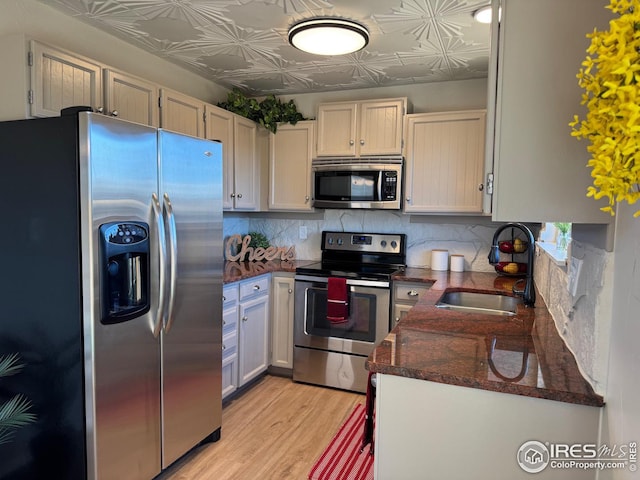 kitchen featuring sink, appliances with stainless steel finishes, backsplash, white cabinets, and light wood-type flooring