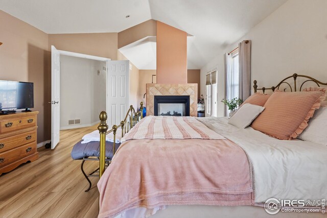 bedroom featuring light hardwood / wood-style flooring, a tiled fireplace, and vaulted ceiling