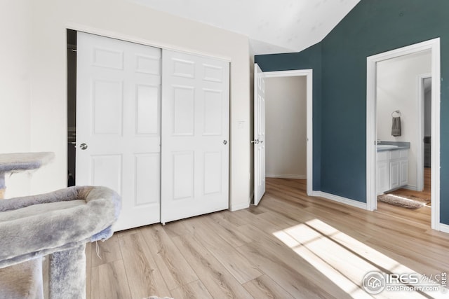bedroom featuring lofted ceiling, ensuite bath, a closet, and light wood-type flooring