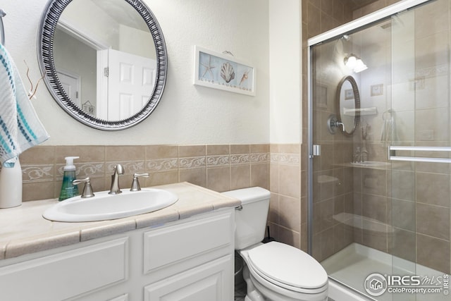 bathroom with an enclosed shower, vanity, toilet, and tile walls