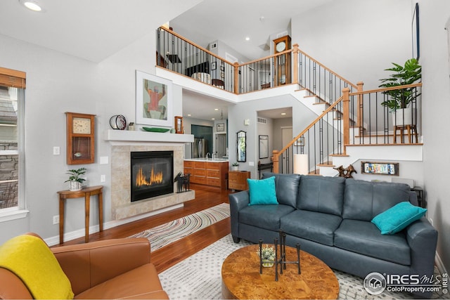 living area with stairs, a tile fireplace, a high ceiling, wood finished floors, and baseboards
