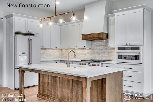 kitchen featuring white cabinetry, custom exhaust hood, hanging light fixtures, a kitchen island with sink, and white appliances