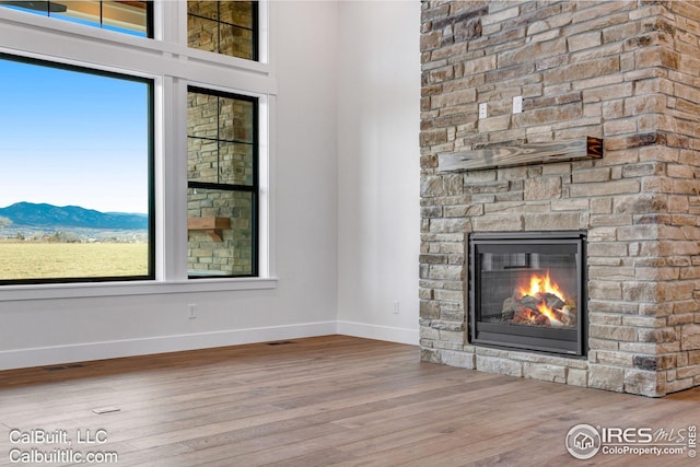 unfurnished living room featuring a mountain view, hardwood / wood-style floors, and a stone fireplace