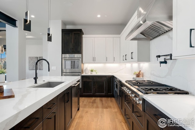 kitchen featuring stainless steel gas cooktop, a sink, light wood-type flooring, wall chimney range hood, and white cabinets