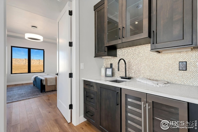 bar featuring wine cooler, a sink, light wood-style flooring, and baseboards