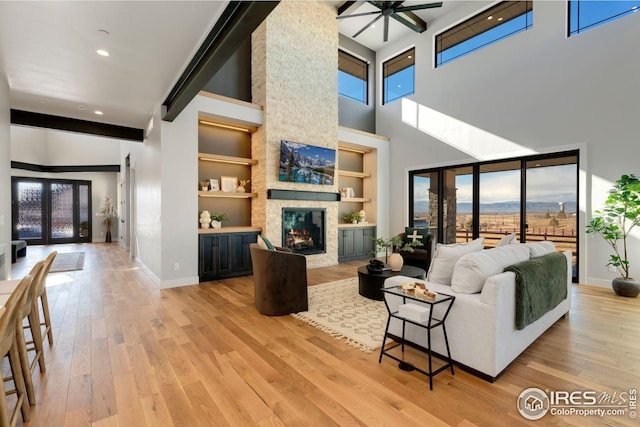 living room featuring a high ceiling, a large fireplace, light wood-style floors, baseboards, and french doors