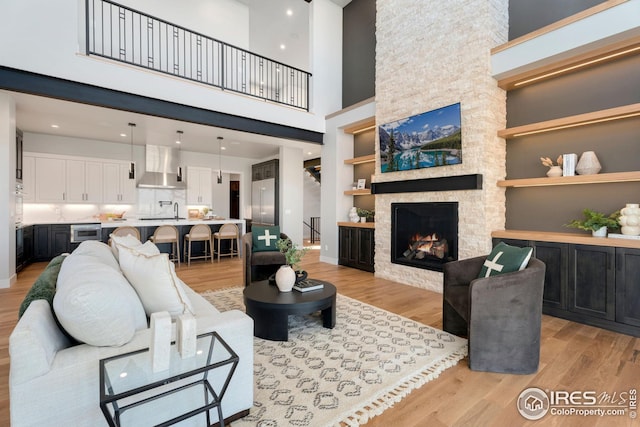 living room with recessed lighting, a high ceiling, built in features, a stone fireplace, and light wood-style flooring