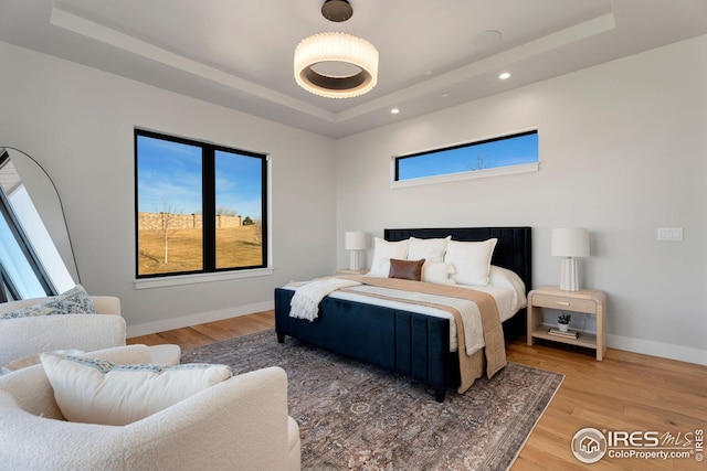 bedroom with multiple windows, light wood-style flooring, and a tray ceiling