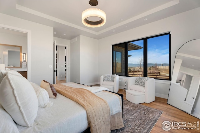 bedroom featuring light wood-type flooring, a tray ceiling, and baseboards