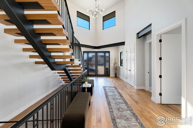 entrance foyer with a chandelier, french doors, baseboards, wood finished floors, and a high ceiling
