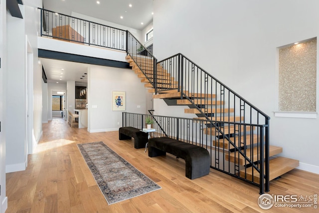 stairway featuring a towering ceiling, wood finished floors, recessed lighting, and baseboards
