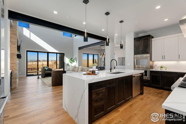 kitchen featuring light wood finished floors, light stone countertops, stainless steel double oven, a sink, and pendant lighting