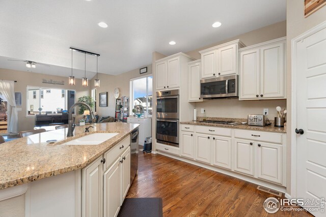 kitchen featuring light stone counters, dark wood-style floors, hanging light fixtures, appliances with stainless steel finishes, and a sink