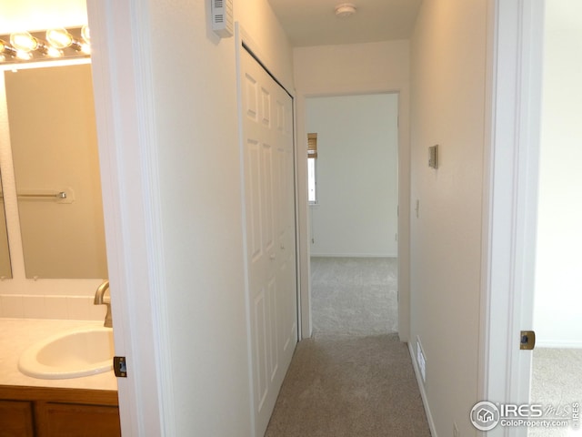 hallway with sink and light colored carpet