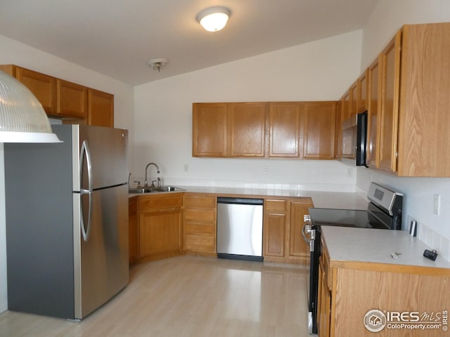 kitchen with lofted ceiling, appliances with stainless steel finishes, sink, and light wood-type flooring