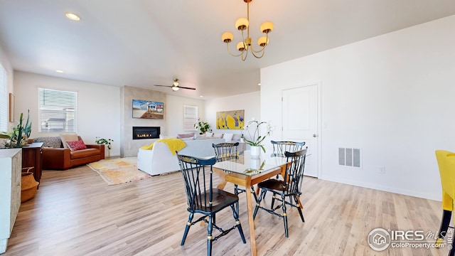 dining room featuring visible vents, a fireplace, light wood-style floors, and ceiling fan with notable chandelier