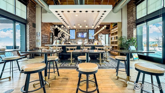 bar with brick wall, plenty of natural light, light wood finished floors, and a towering ceiling